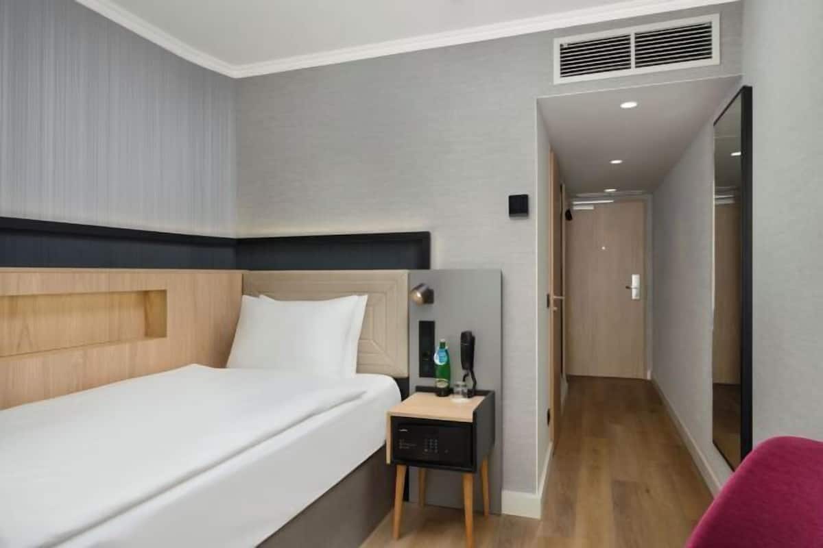 Una habitación de hotel con cama, mesita de noche y espejo.