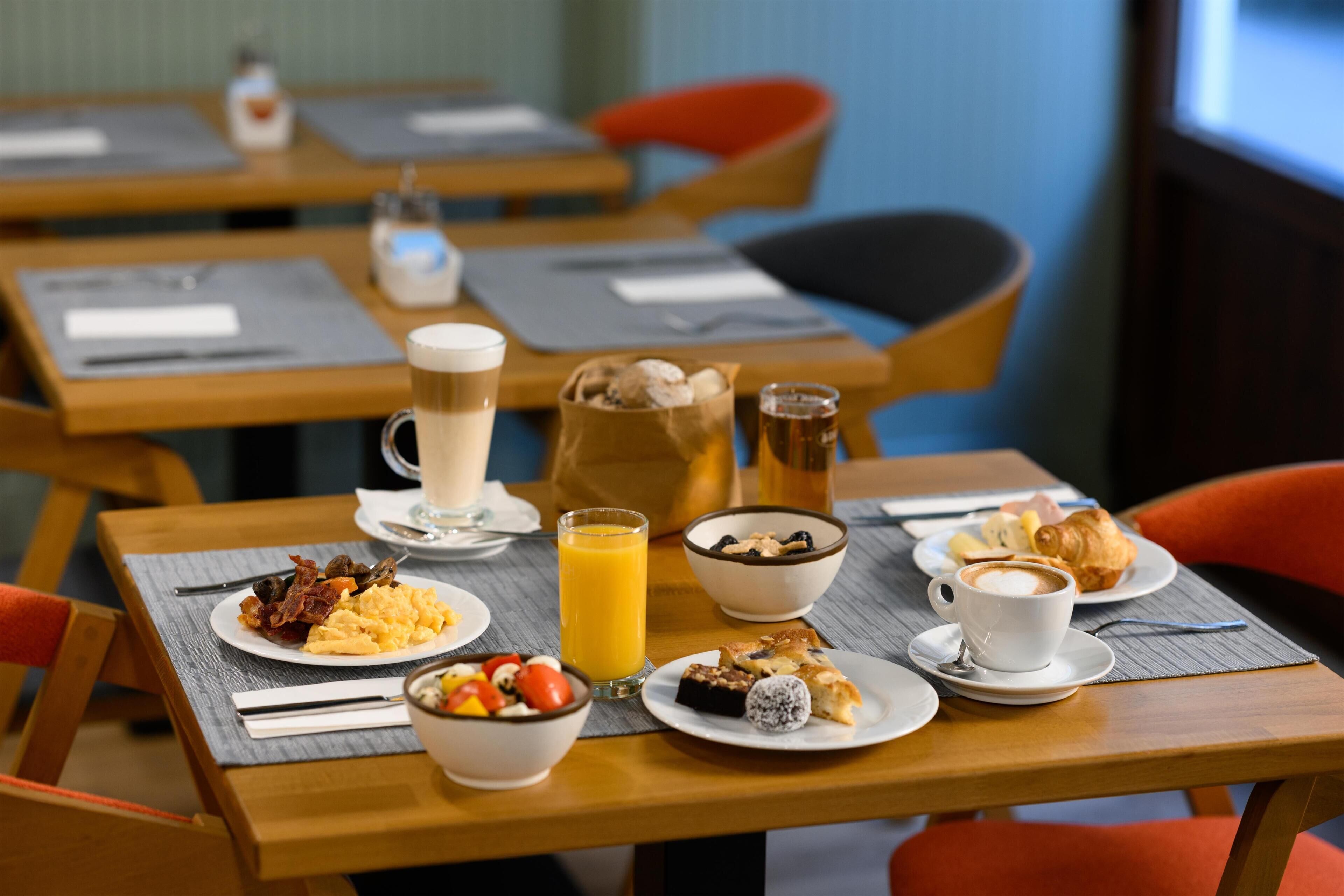 A breakfast setting with various dishes, a coffee cup, and a juice glass on a table.