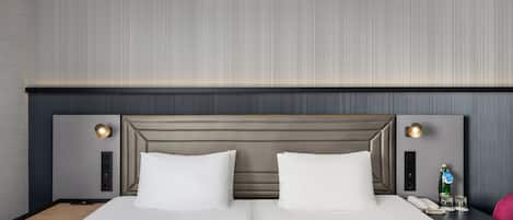 Habitación de hotel con una cama grande, dos mesitas de noche, una lámpara, una botella de agua y una silla.