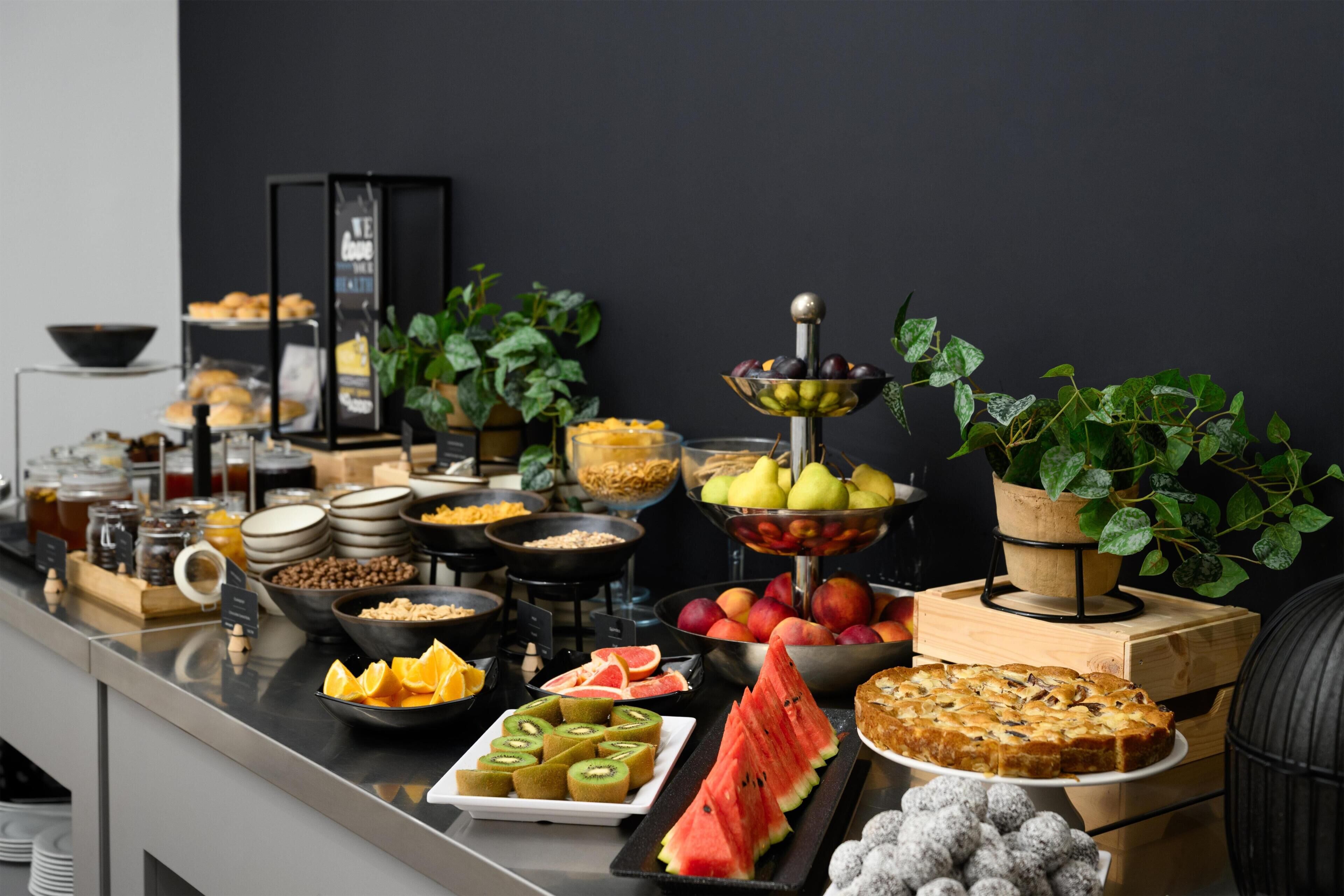 A buffet with various food items including fruits, pastries, and beverages.