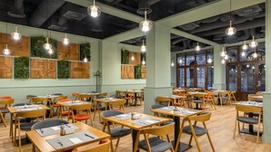 A spacious dining area with multiple tables and chairs, wooden panel walls, and hanging pendant lights.