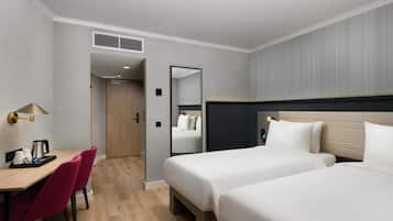 Habitación de hotel con dos camas, un escritorio con cafetera y un espejo.