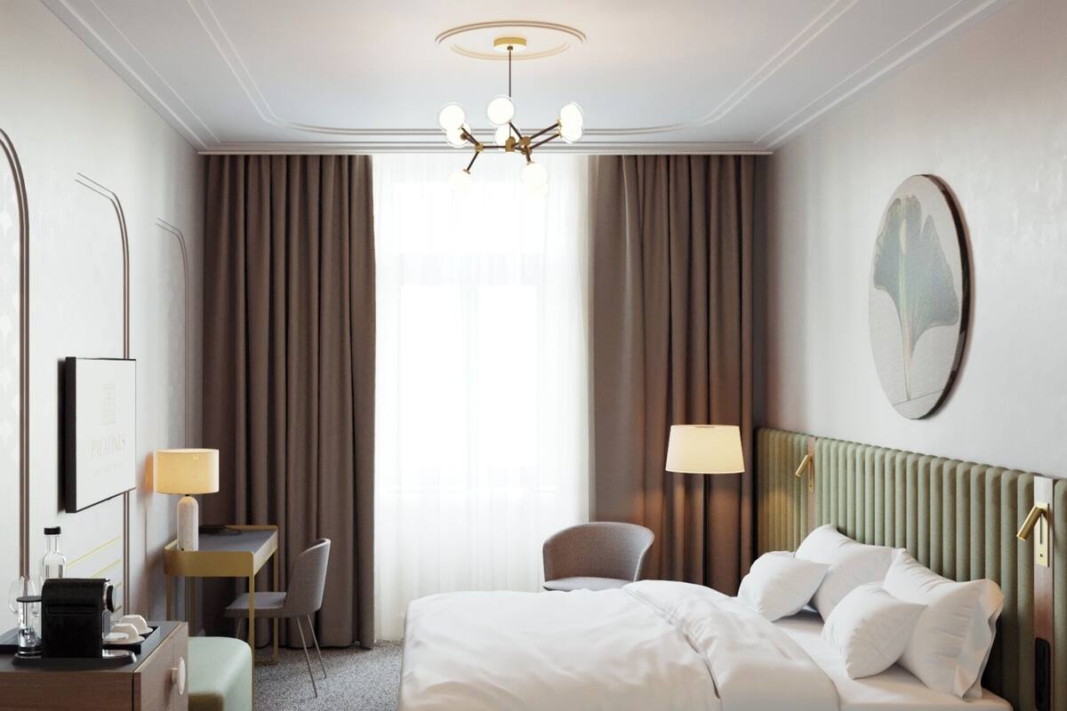 A hotel room with a bed, a desk, a chair, a lamp, and a mirror.