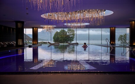 Piscina infinita en el interior con vistas al océano y a las montañas, rodeada de arquitectura moderna y una lámpara colgante única.