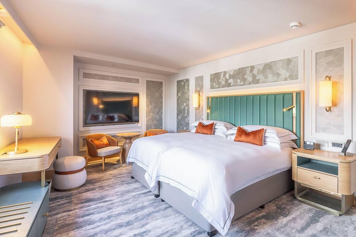 A hotel room with a large bed, a desk, a TV, and a seating area.