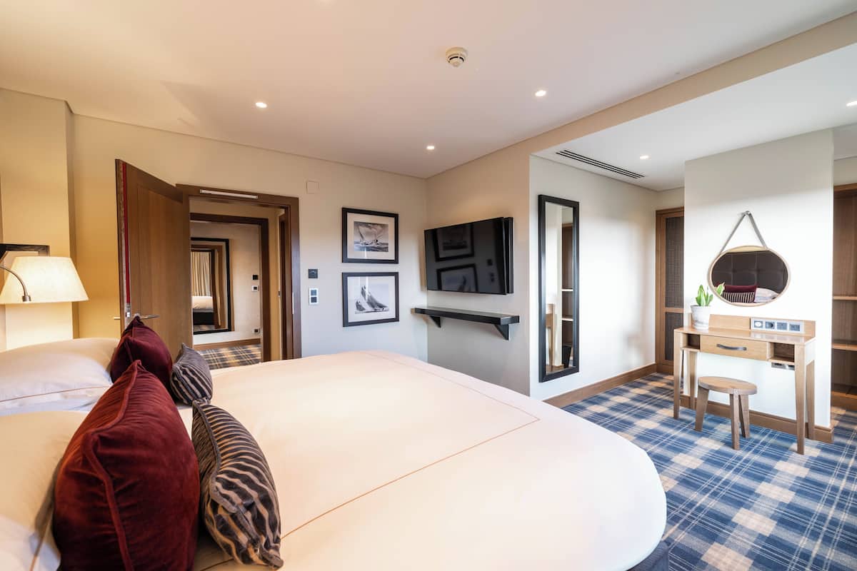 A hotel room with a large bed, a desk, a chair, a lamp, and a television.