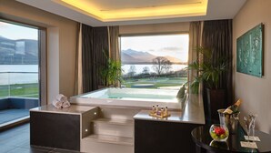Een moderne badkamer met een bad, een zithoek en uitzicht op een meer en bergen.