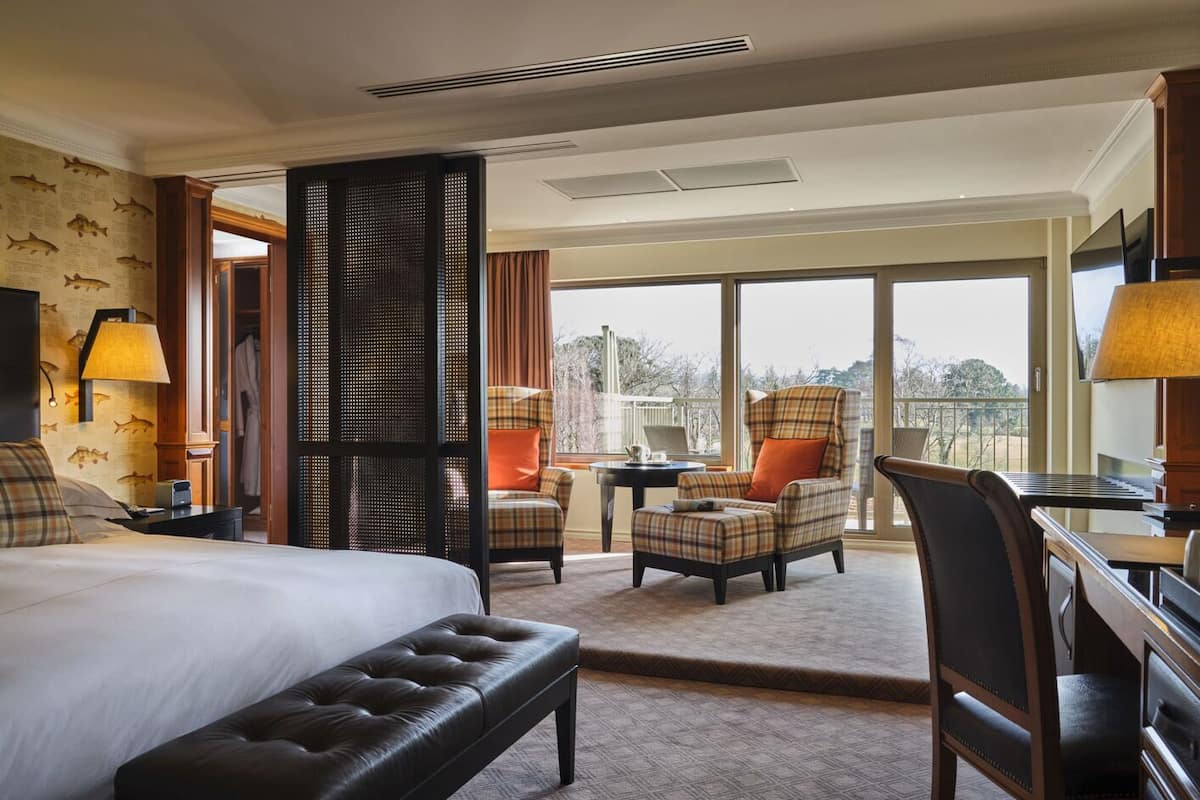 A hotel room with a large bed, a desk, a chair, and a balcony with a view.