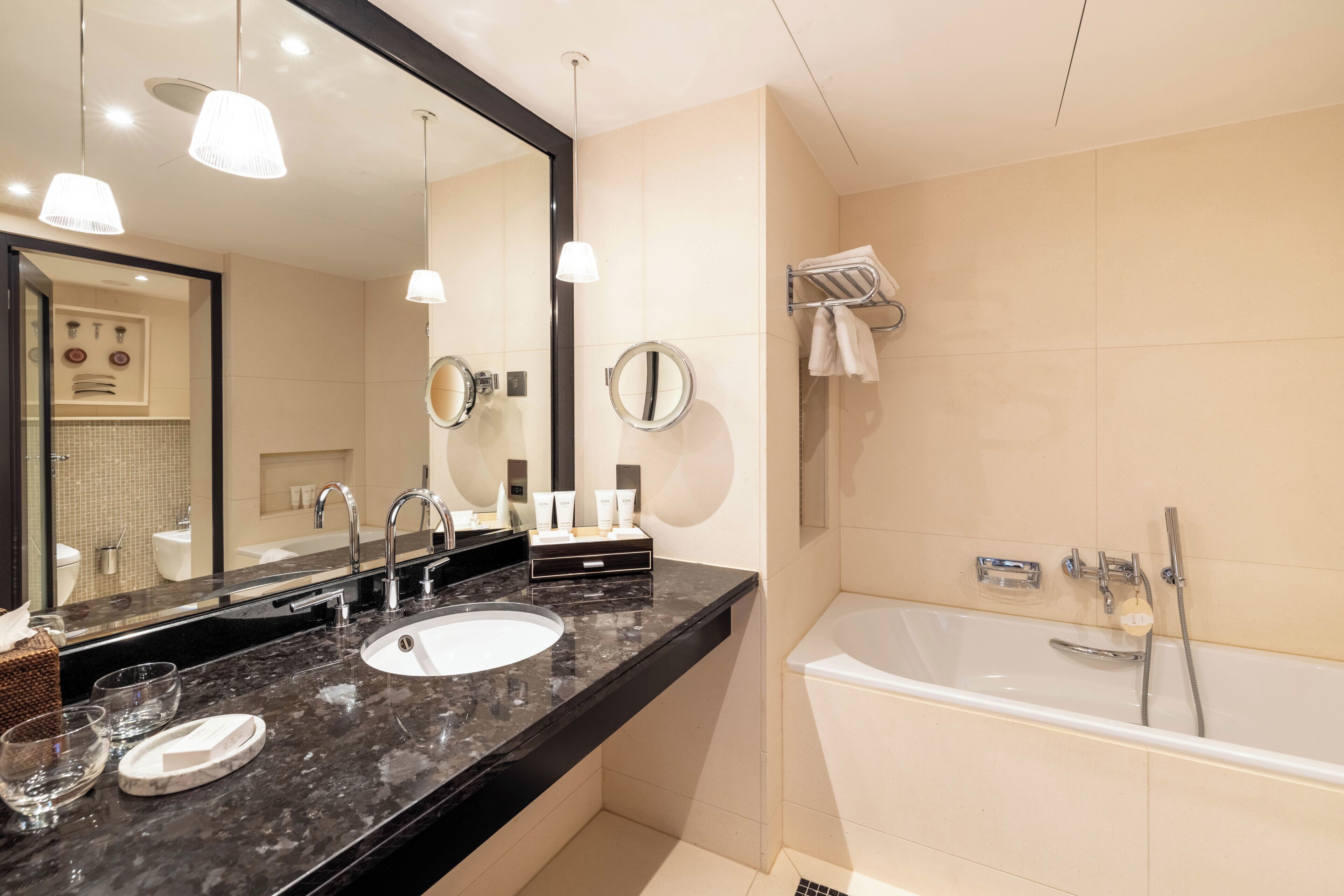 A modern bathroom with a black marble sink, a large mirror, and a separate bathtub.