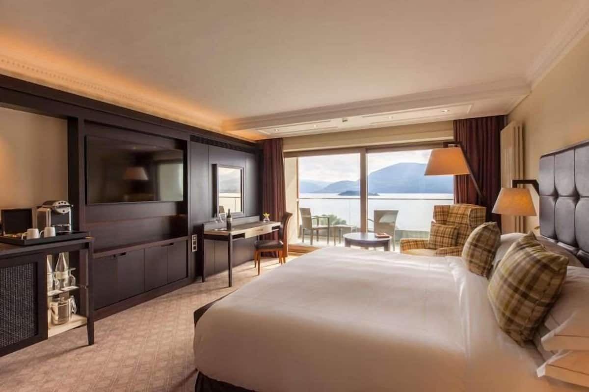 A hotel room with a large bed, a desk with a chair, a TV, and a view of the sea.