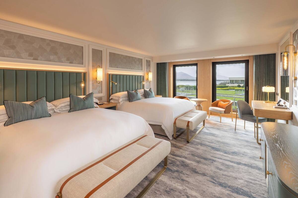 A hotel room with two beds, a desk, a chair, and a view of a body of water.