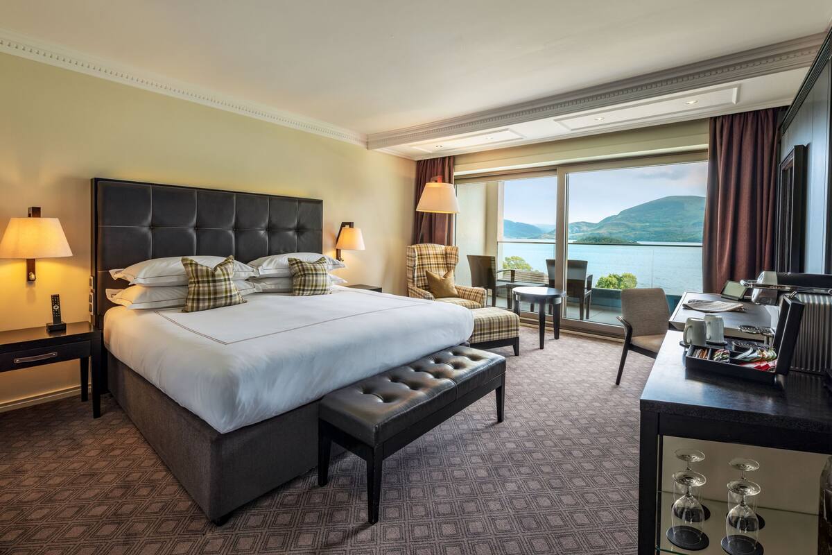 A hotel room with a large bed, a desk, a chair, and a view of a lake.