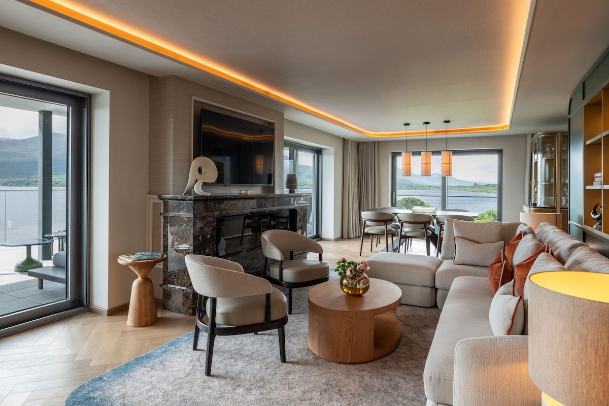 A modern living room with a fireplace, comfortable seating, and a large window overlooking a body of water.