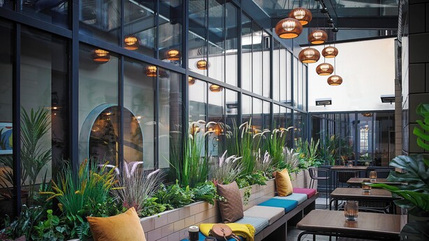 An indoor seating area with cushioned benches, tables, and hanging pendant lights. - The Mont (Dublin)