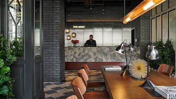 Un espace d’accueil moderne comprenant un comptoir de réception, un réceptionniste et un coin salon avec des chaises et des tables.