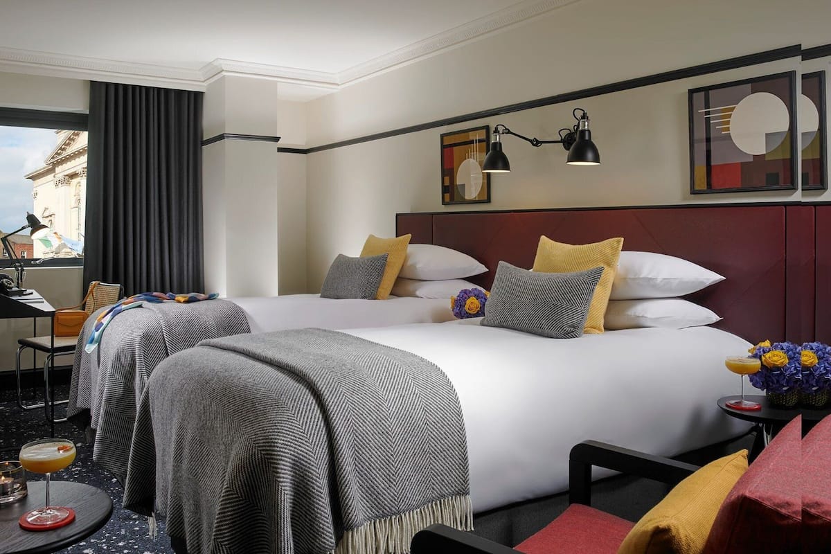 Quarto de hotel com duas camas, uma mesa e janela com cortinas.