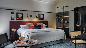 A modern hotel room with a large bed, a round coffee table, a chair, and a bookshelf.