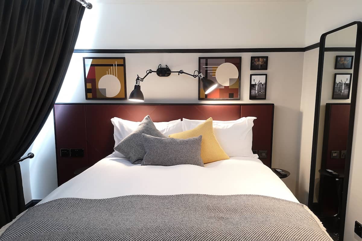 Quarto de hotel com uma cama grande, cabeceira com espelho e obras de arte na parede.
