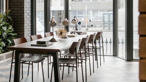 A modern dining area with a large table and chairs, a potted plant, and a view of the street through large windows. - The Mont (Dublin)