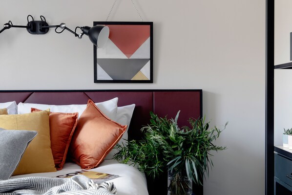 A neatly arranged bedroom with a bed, pillows, a hanging lamp, and a framed picture on the wall.