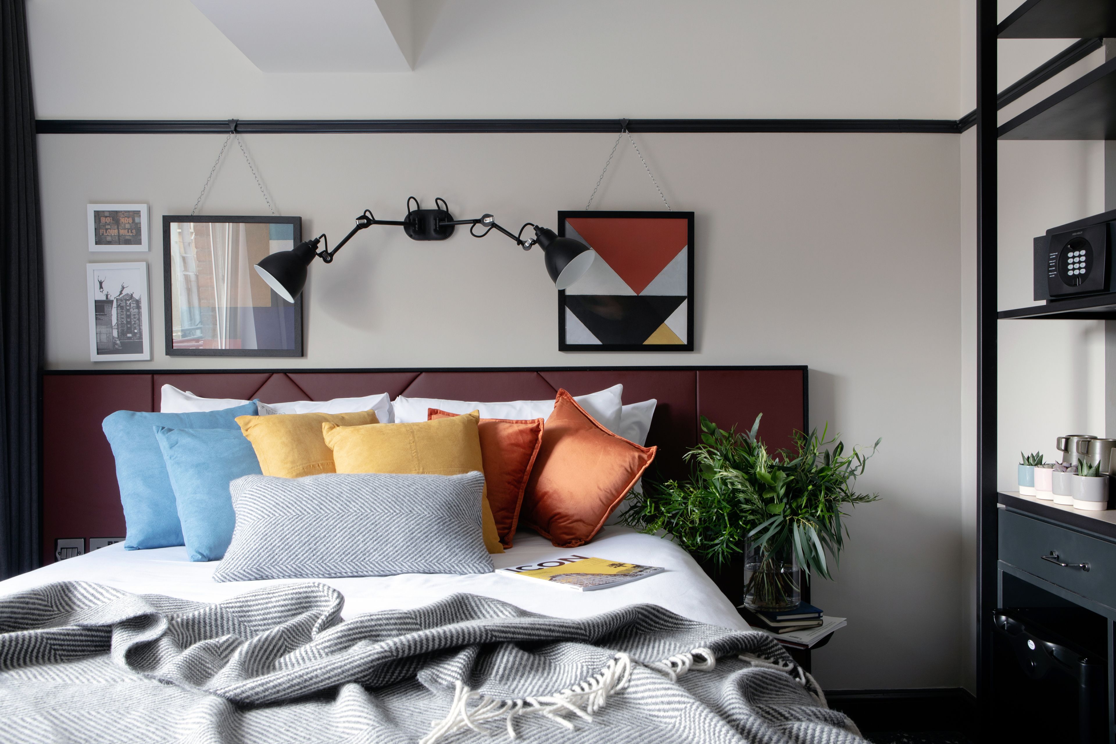 Une chambre à coucher moderne avec un lit soigneusement fait, une tête de lit ornée de motifs géométriques et une plante sur la table de chevet.