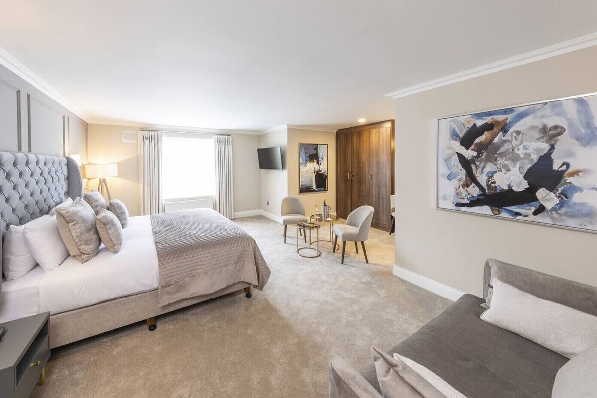 A hotel room with a large bed, a desk, a chair, a TV, and a painting on the wall.
