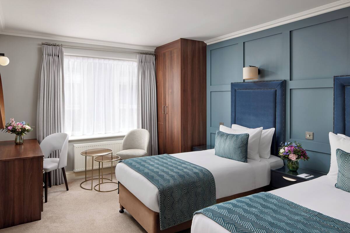 A hotel room with two beds, a desk, a chair, and a window with curtains.