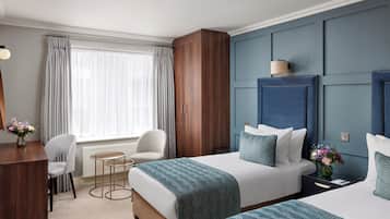 A hotel room with two beds, a desk, a chair, and a window with curtains.