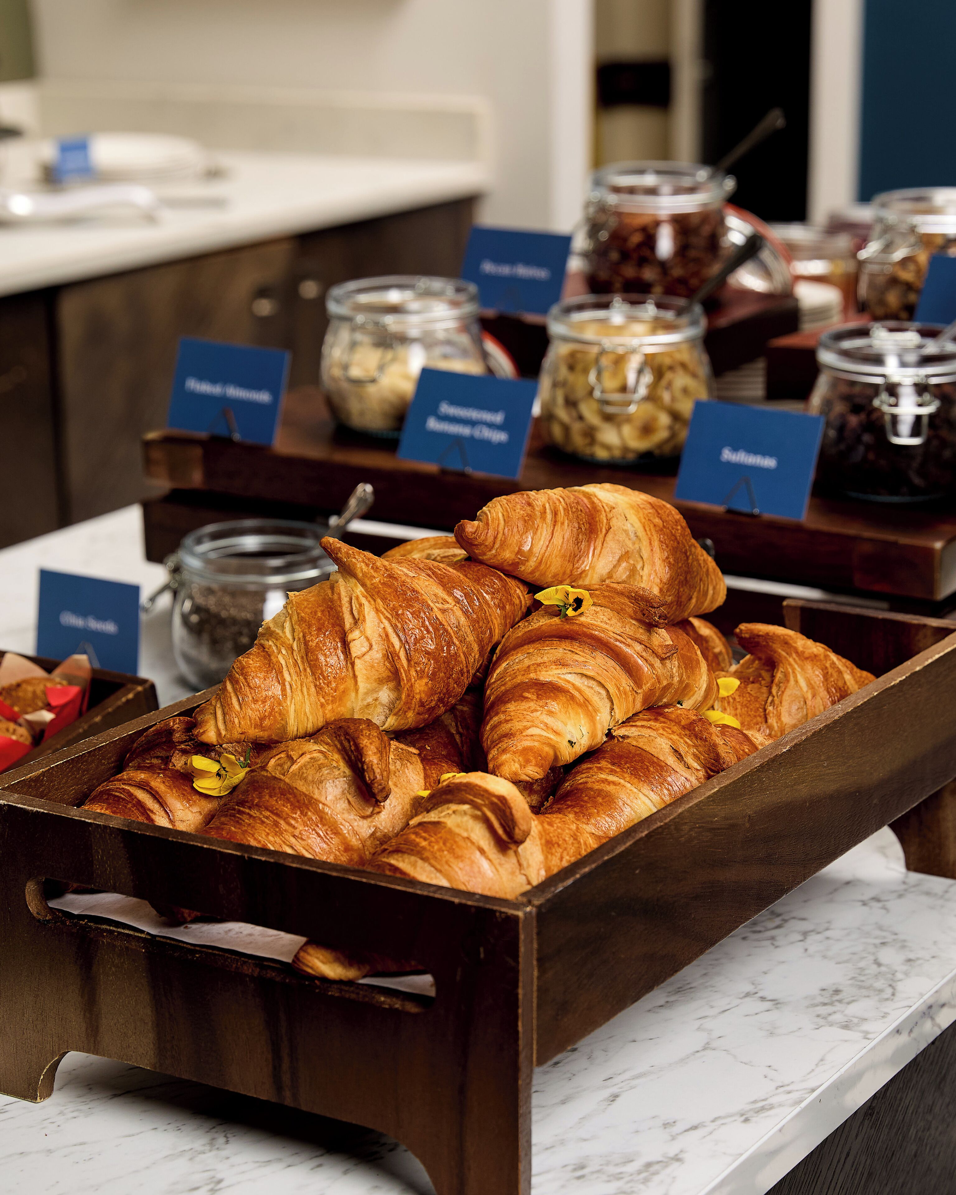 A breakfast buffet with croissants and labeled jars of spreads.