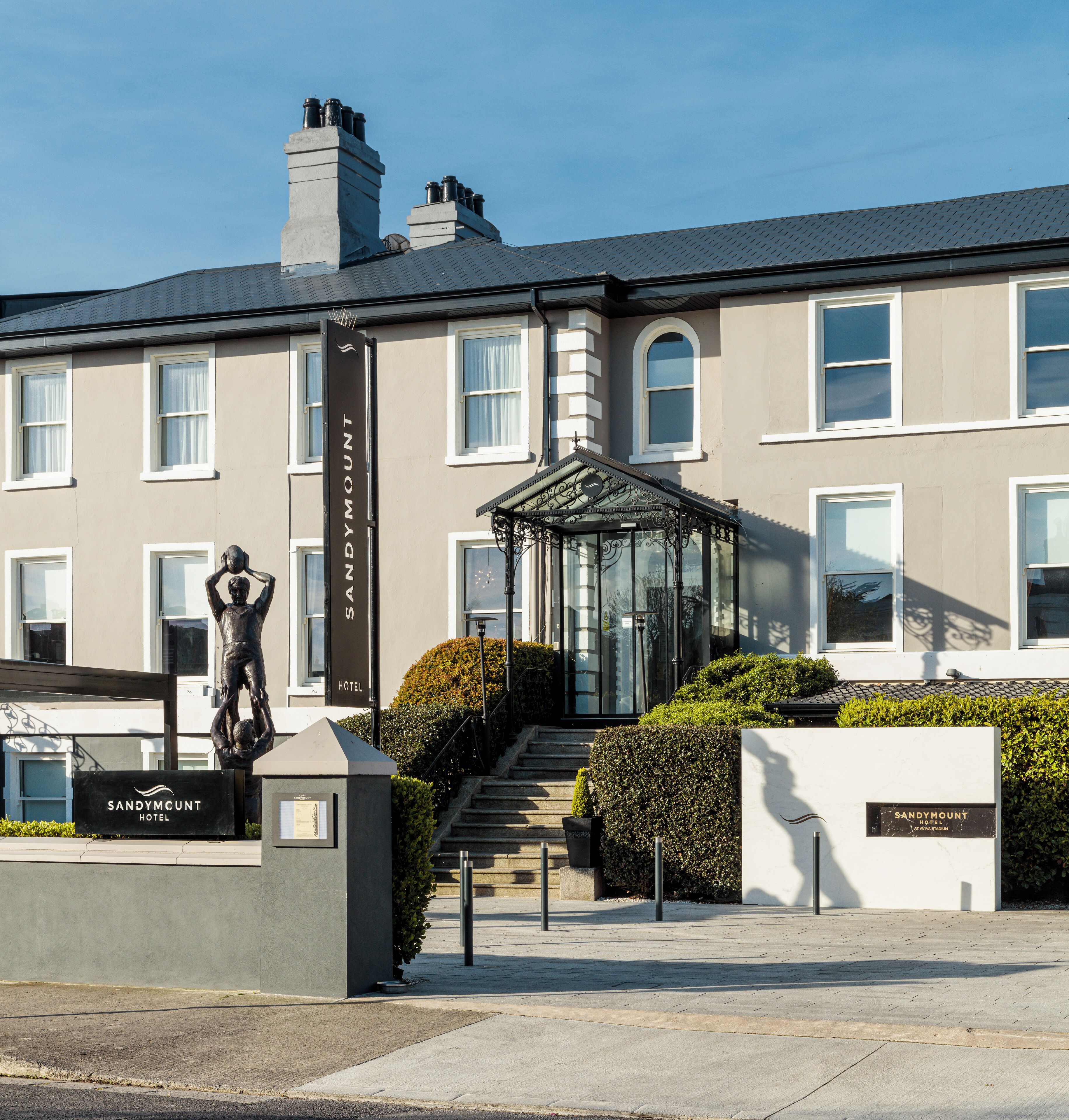 Entrada de hotel con una estatua, un pabellón de vidrio y un letrero que dice "Sandymount Hotel".