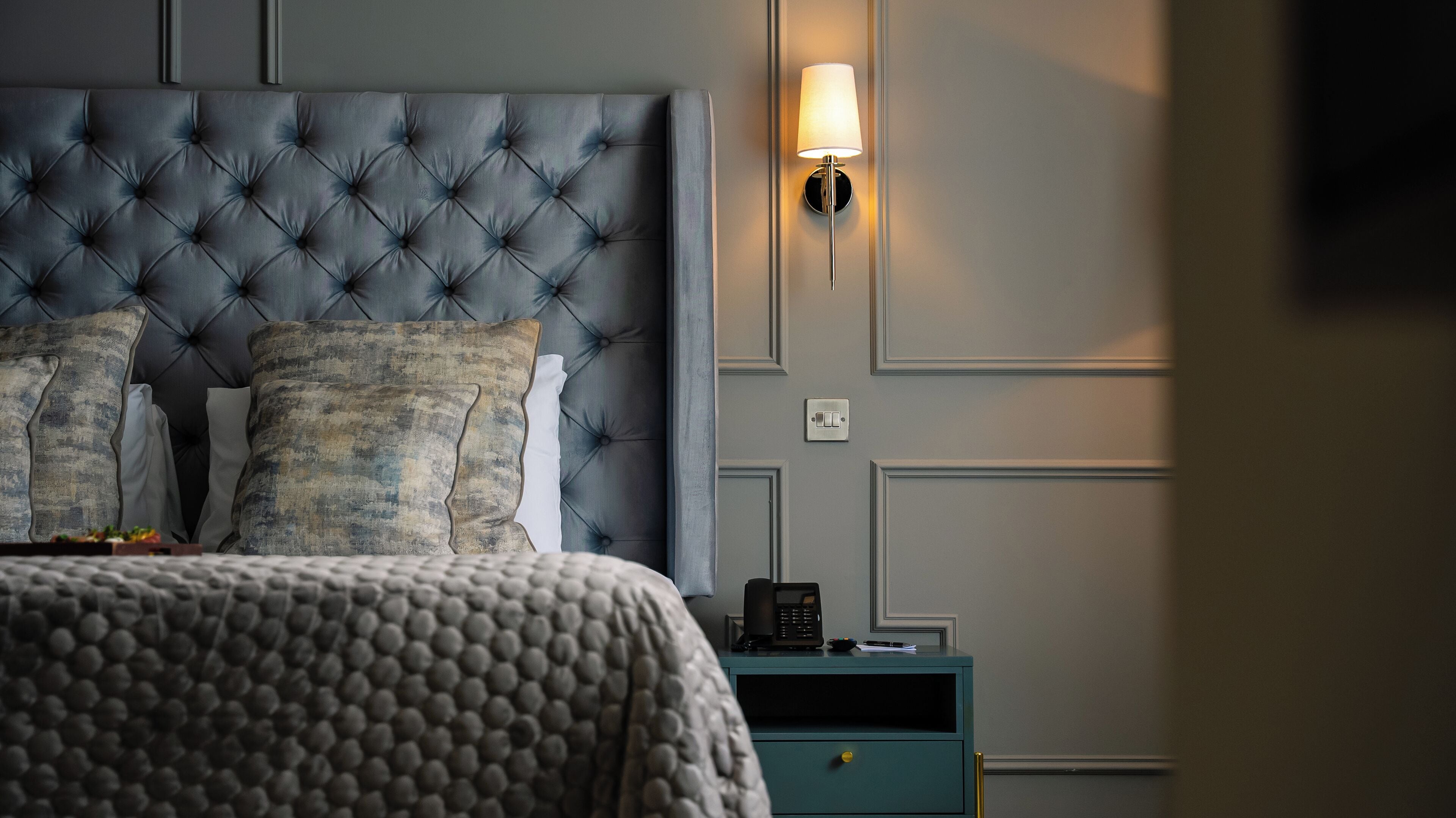 A bedroom with a tufted headboard, a bedside lamp, a telephone, and a nightstand.