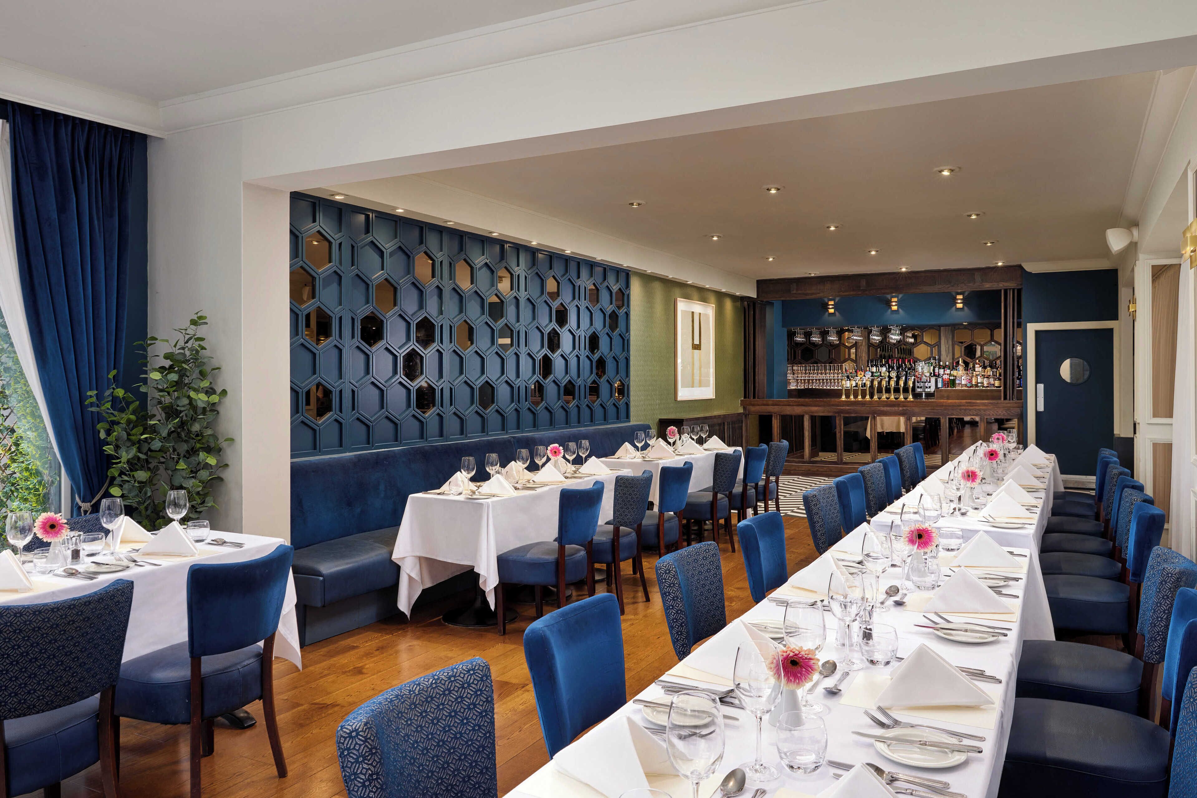 A restaurant with long tables, blue chairs, and a bar area.