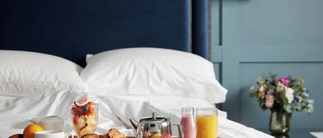 A neatly made breakfast tray on a bed with a variety of food items, a teapot, and a glass of orange juice.