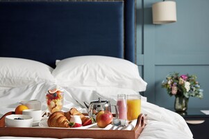 Un plateau de petit-déjeuner bien préparé est posé sur le lit, avec une variété d’aliments, une théière et un verre de jus d’orange.