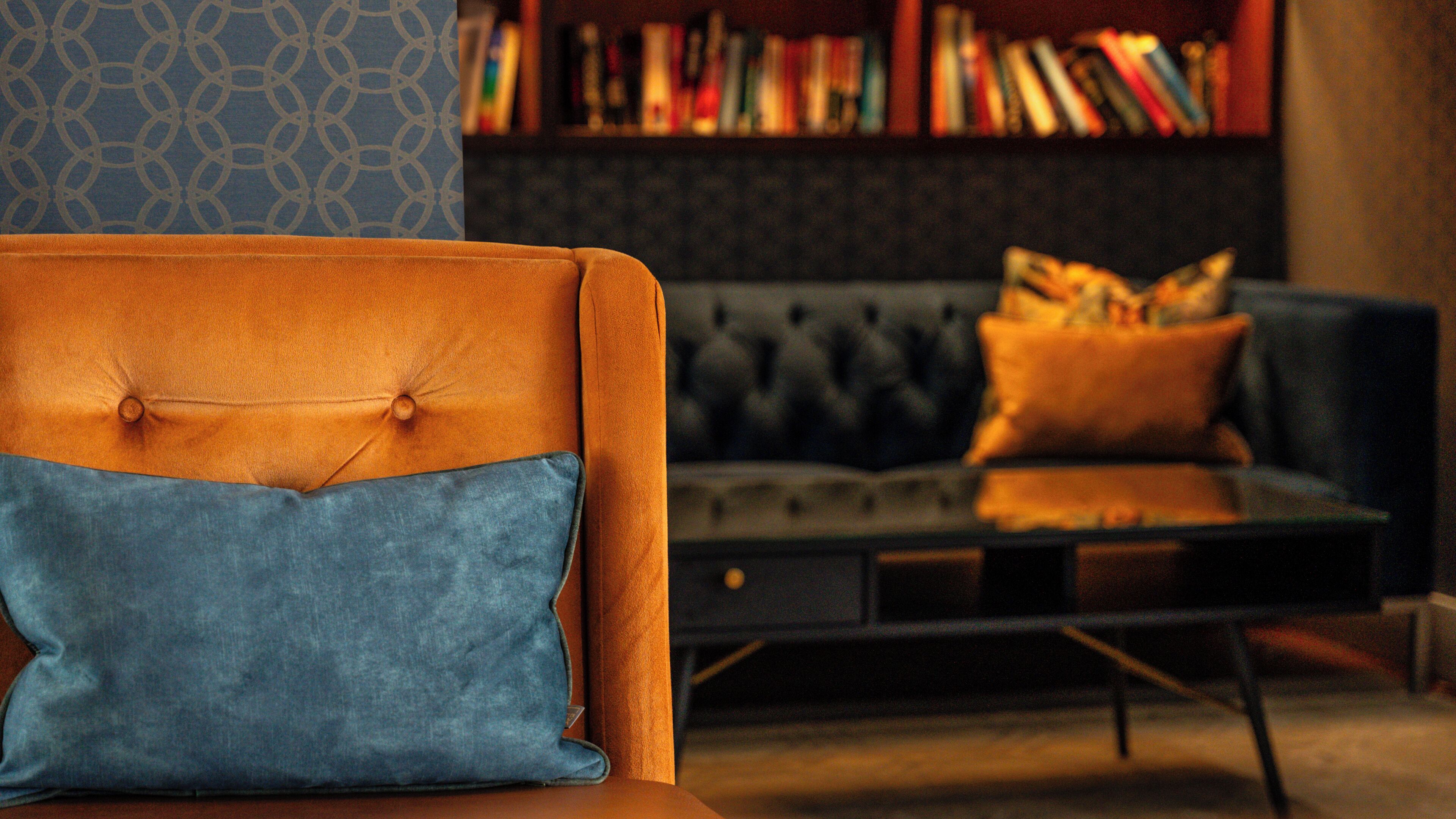 A modern living room with a tufted sofa, a blue pillow, and a bookshelf filled with books.