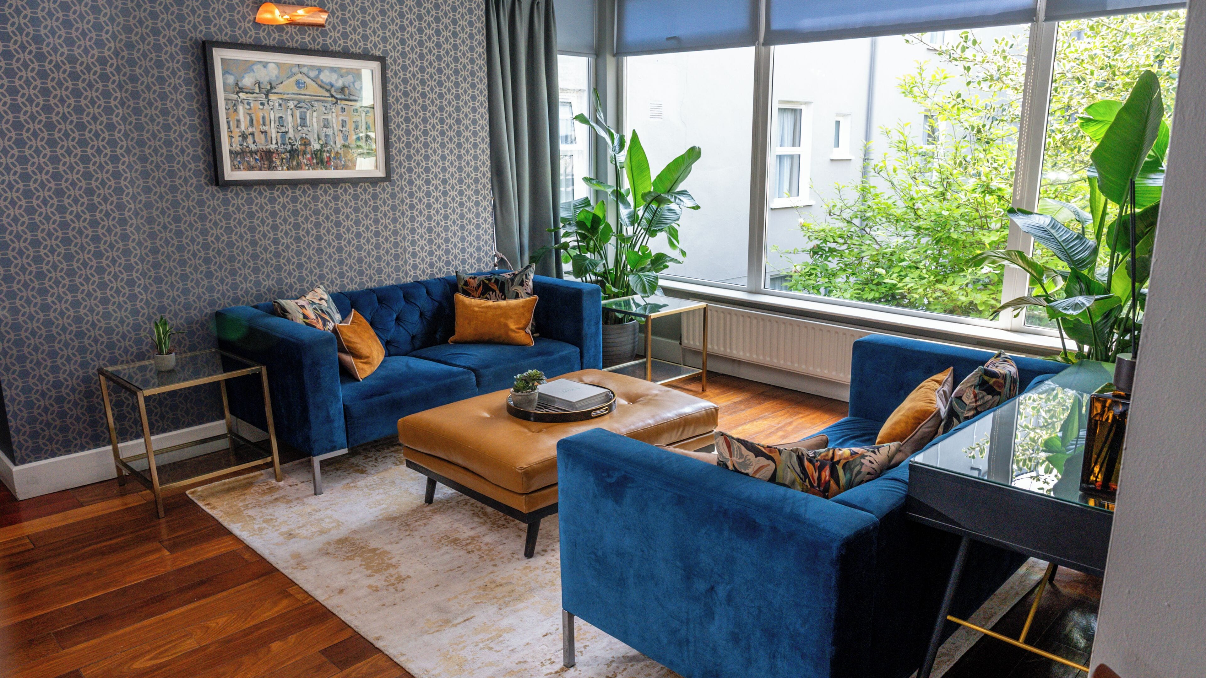 Una sala de estar moderna con un sofá azul, una mesa de centro y vistas a la vegetación exterior.