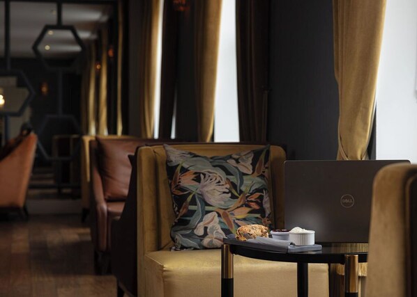 A modern hotel room with a laptop on a small table, a floral pillow on a sofa, and a view of the corridor. - The Sandymount Hotel (Dublin)
