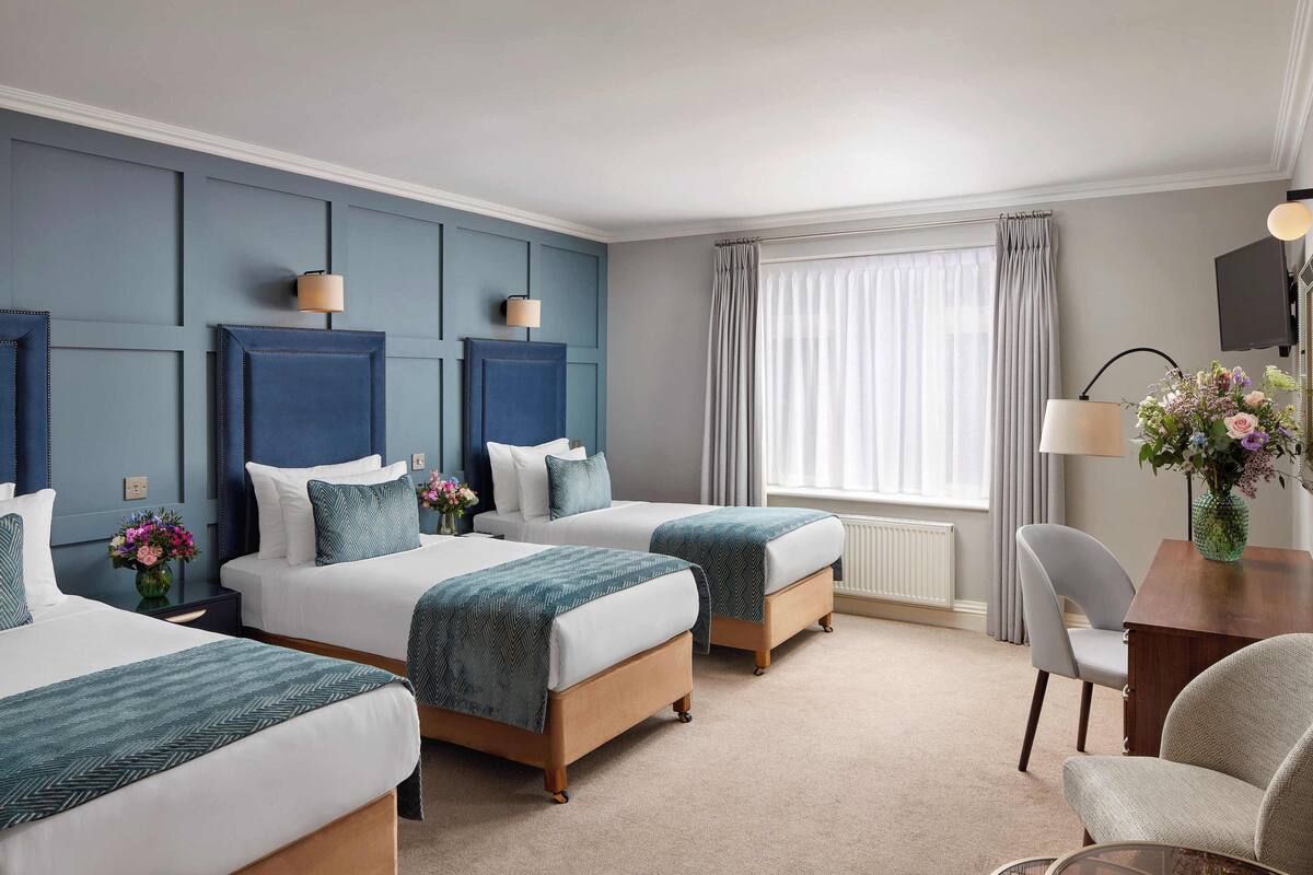 A hotel room with three beds, a desk, and a chair.