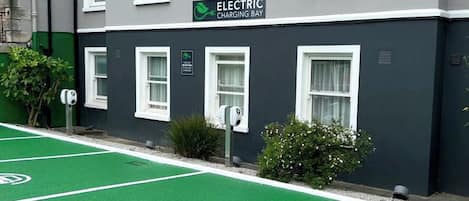 Un edificio con un letrero que dice 'Electric Charging Bay' y una zona de estacionamiento verde con símbolos de vehículos eléctricos.
