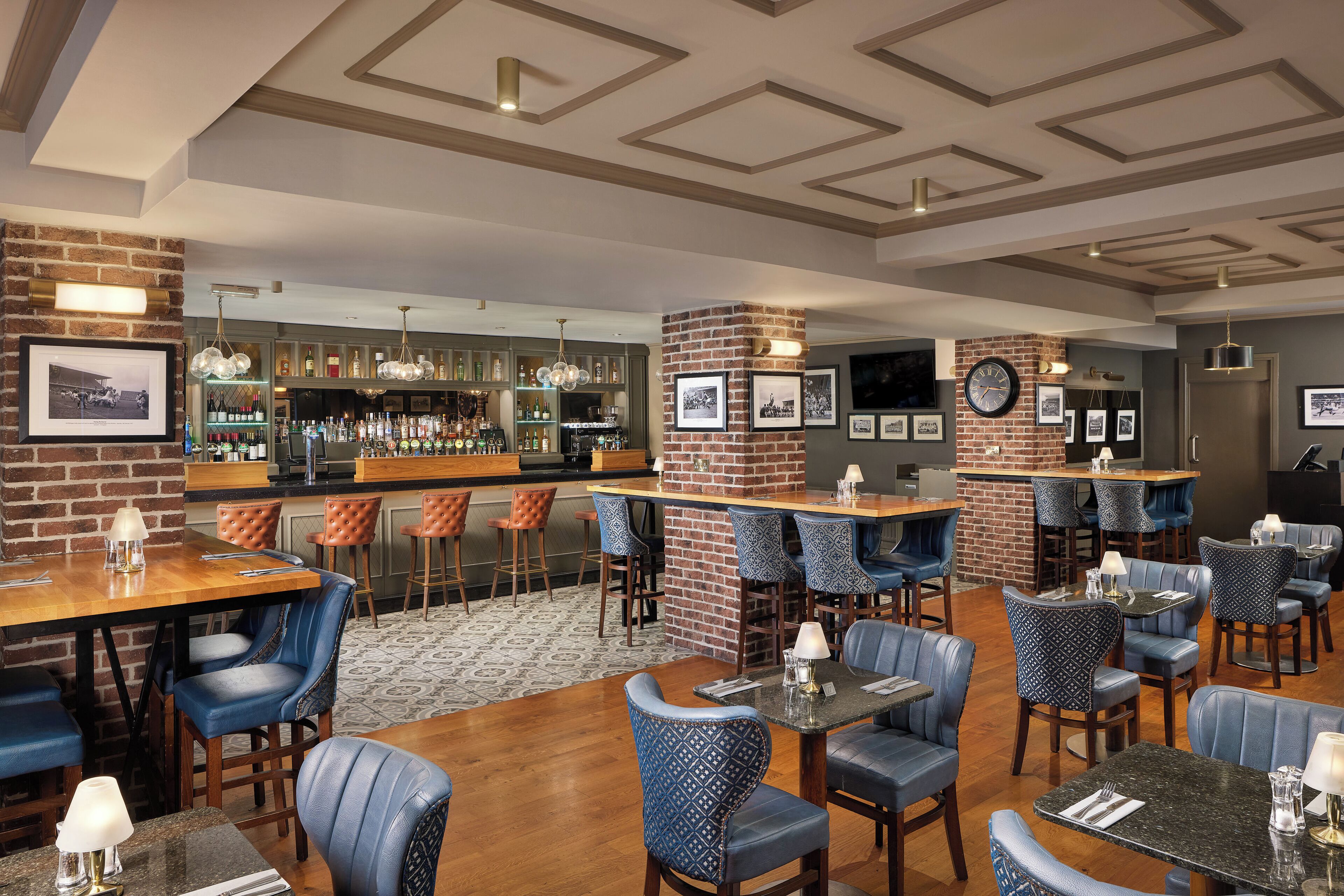 A bar area with multiple seating options, a brick accent wall, and a bar counter with a variety of bottles.