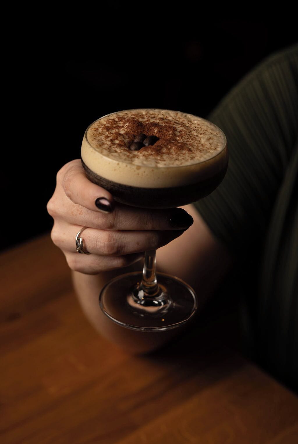 Una persona sosteniendo una copa de cóctel con una bebida en capas, posiblemente un martini, adornada con una pizca de especias.