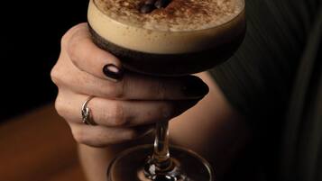 A person holding a cocktail glass with a layered drink, possibly a martini, garnished with a sprinkle of spices.