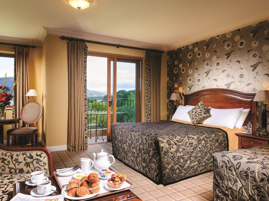 A hotel room with a bed, a dining table with breakfast, a chair, and a view of the outdoors.