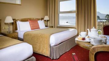 A hotel room with two beds, a dining table with tea set, and a view of a lake.
