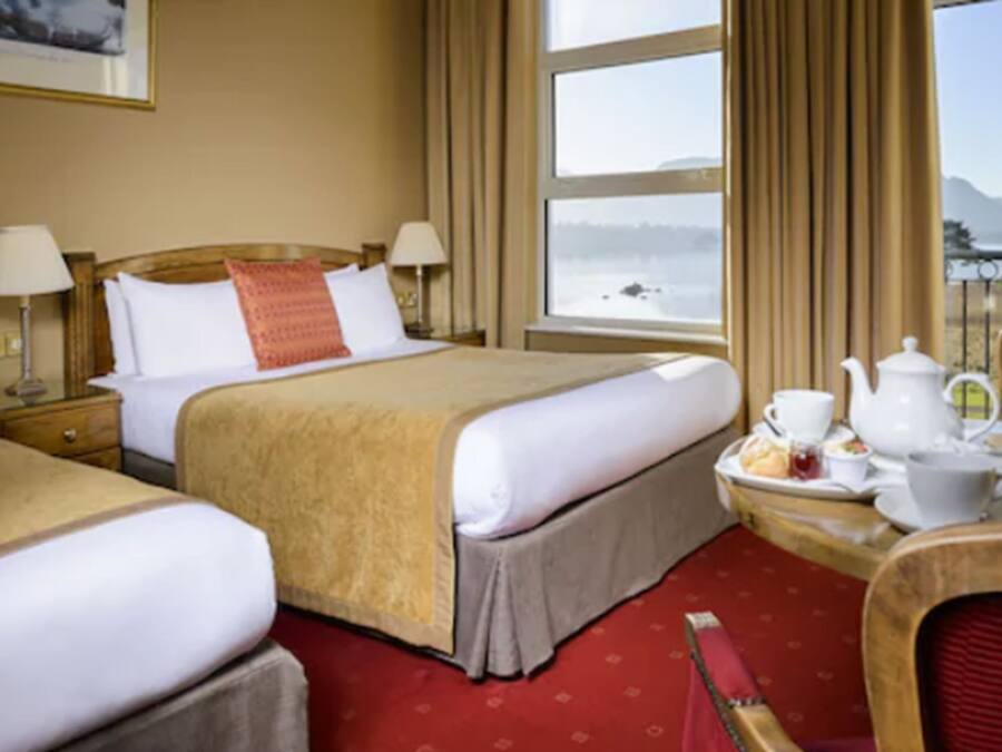 A hotel room with two beds, a dining table with tea set, and a view of a lake.