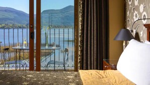 Camera d'albergo con balcone vista su lago e montagne.