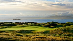 Un campo da golf con vista sull'oceano e montagne in lontananza.