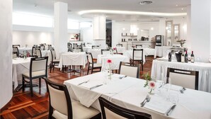 A restaurant with multiple tables set for dining, featuring white tablecloths and chairs. - Hotel Carlo Felice (Sassari)
