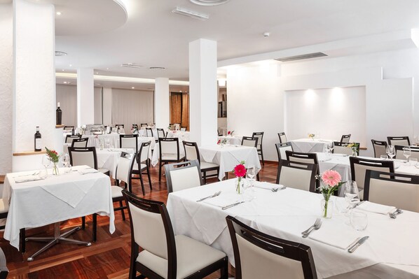 A spacious dining area with multiple tables and chairs, white tablecloths, and floral centerpieces.