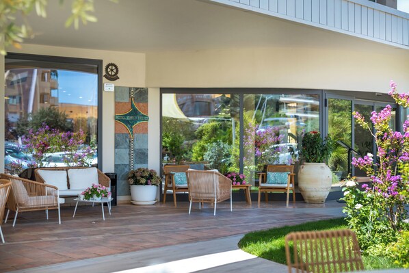 Fachada moderna de un hotel con asientos exteriores, ventanas amplias y un jardín.